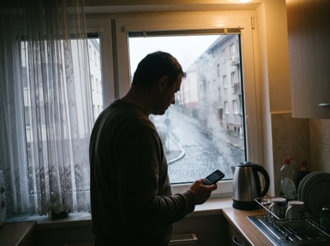 Ruce drží mobil u okna v rozostřené dílně, na displeji jen pár bledě šedých zaoblených bloků a jeden tlumený barevný pru